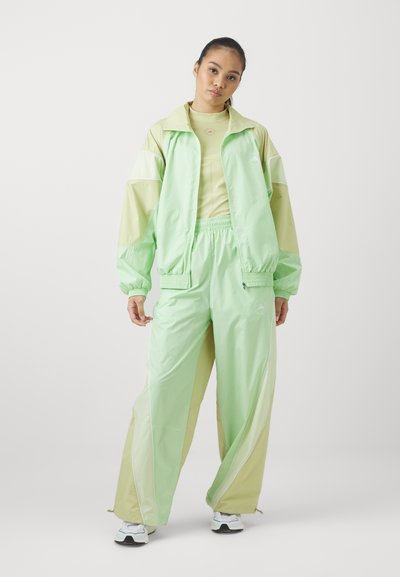 Survêtement vert clair avec des panneaux contrastants vert pâle. Fabriqué en tissu synthétique lisse, doté d'une taille élastique et d'un design sportif.