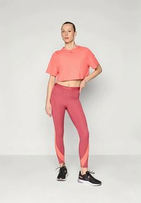 Hele roosa lühikeste varrukatega lühike T-särk, mis on kombineeritud sobivate burgundia värvi retuusidega, millel on oranžid aktsendid, ja mustade sportlike kingadega.