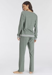 Grünes Loungewear-Set bestehend aus einem Langarmoberteil mit Rundhalsausschnitt und kontrastierenden weißen Streifen an den Bündchen und dem Saum, kombiniert mit passenden Hosen.