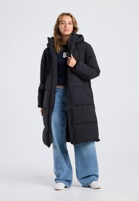 Black puffer coat with a hood, featuring a quilted design and front zipper. Paired with light blue wide-leg jeans and white sneakers.