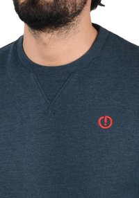 Marineblauwe sweatshirt van een katoenmix, met een gestructureerde v-hals en een klein rood geborduurd logo op de linkerborst.