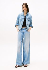 Chaqueta de denim azul claro con mangas enrolladas, combinada con pantalones de denim de talle alto y pierna ancha a juego y sandalias negras. Top negro debajo.