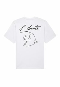Witte katoenen T-shirt met een zwarte omtrek van een duif en het woord "Liberté" in een vloeiende schrift op de rug. Korte mouwen, ronde hals.