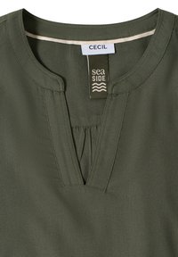 Blouse vert olive avec un col rond, un détail plissé et une étiquette portant les inscriptions "Cecil" et "sea SIDE." Tissu lisse avec une légère brillance.