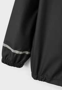 Zwarte waterdichte jas met elastische manchetten, voorzien van een reflecterende grijze streep langs de mouwen. Glad textuur met een licht glanzende afwerking.