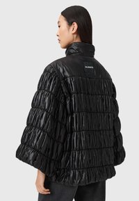 Svart vadderad jacka med ett glänsande, quiltat mönster och överdimensionerad silhuett. Har en hög krage och en logotypmärke på baksidan.