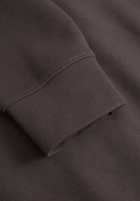 Dark brown sweatshirt fabric with a ribbed cuff and smooth texture. Features a clean finish without visible seams on the cuff.