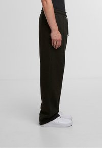 Dark green sweatpants with an elastic waistband and drawstring, made from soft fabric. Paired with white sneakers. Side view.