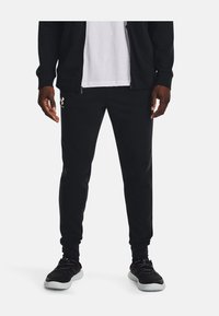 Mustad mustad püksid, mis on pehme ja slim-fit lõikega, realt paelaga vöö, küljetaskud ja diskreetne logo vasakul reitel. Pehme kangastekstuuri.