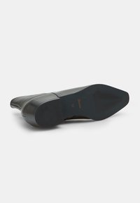 Botín de piel negra hasta el tobillo con puntera redondeada y un tacón bajo en bloque. La suela está texturizada con surcos para mayor tracción. Talla 37 visible en el interior.
