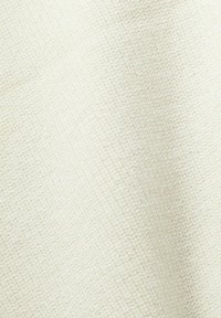 Gros plan d'un tissu en tricot de couleur crème avec un motif en côtes diagonales et une texture douce.