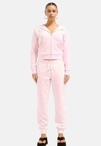 Różowy dres z weluru składający się z bluzy z zamkiem błyskawicznym i pasujących spodni dresowych, z ściągaczami przy mankietach, elastycznym pasem na sznurki i błyszczącymi akcentami.