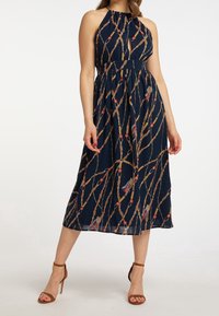 Marinblå halterneck-klänning med en öppen nyckelhålsdesign, prydd med ett guld kedjemönster och färgglada accenter. Knälång med en utsvängd kjol.