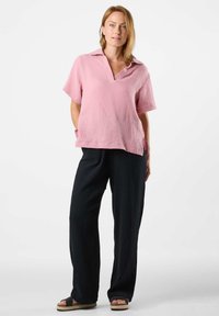 Haut rose texturé à manches courtes avec un col, associé à un pantalon large noir. L'ensemble présente une coupe décontractée et un style casual.