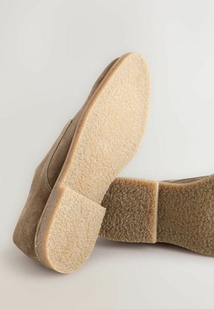 Chaussure en daim marron avec une semelle en caoutchouc beige clair texturée. Le talon est plat et plus large, avec des bords lisses et des détails subtils.