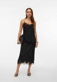 Vestido de satén negro con borde de encaje, presenta un top ajustado con tirantes finos, falda fluida y detalles de encaje en el dobladillo. Incluye un bolso de mano.