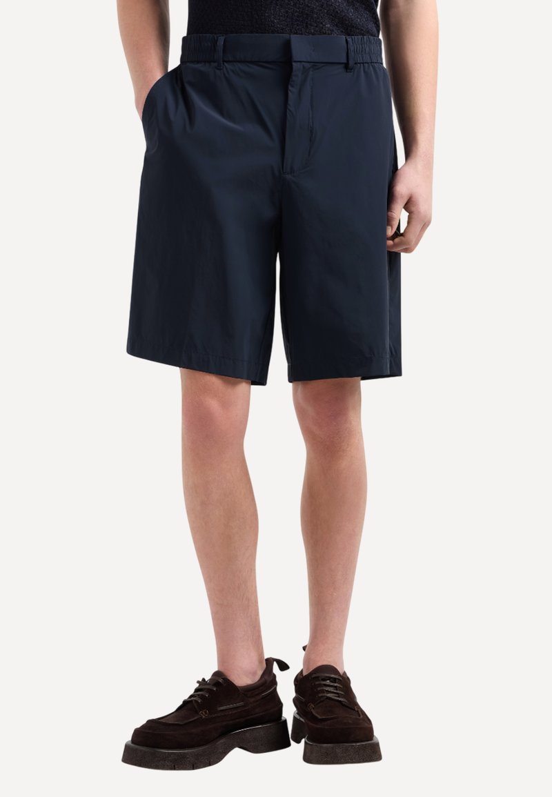 Pantaloni corti blu navy realizzati in tessuto leggero, con una cintura elastica, tasche laterali e una vestibilità morbida, che terminano poco sopra il ginocchio.