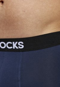 Mörkblå kalsonger med svart elastiskt midjeband med vit text "SOCKS". Slät yta med synliga söm detaljer.