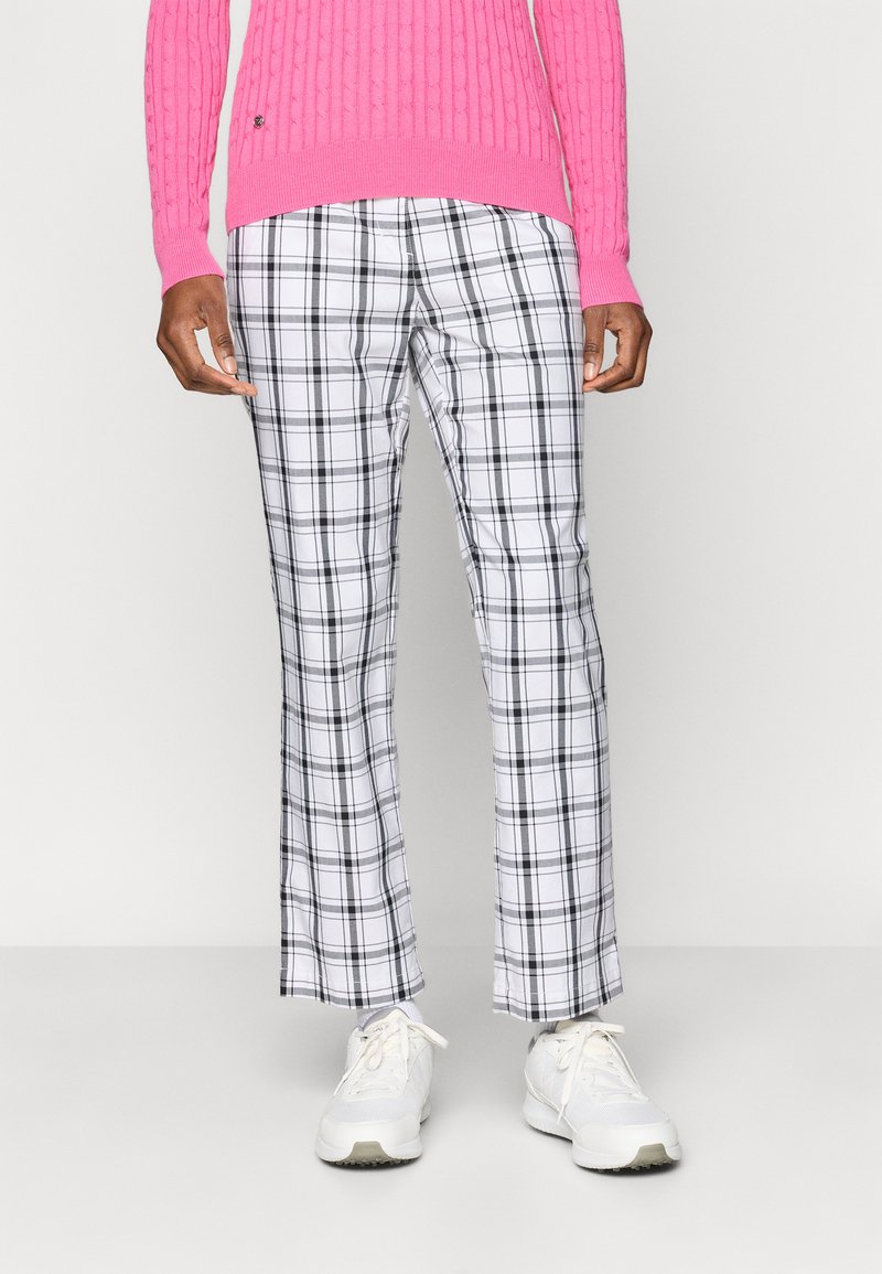 Hvite og svarte rutete bukser med rett passform, kombinert med en rosa ribbestrikket genser og hvite sneakers. Glatt stofftekstur.