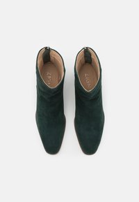 Botas de tobillo de ante verde con punta afilada, cremallera lateral y forro interior suave. Presentan un diseño corto y estructurado.