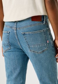 Jasnoniebieskie dżinsy z klasycznym pięciopocketowym fasonem, z subtelnymi detalami szwów oraz brązową skórzaną metką marki na pasie.