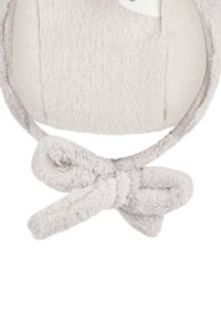 Soft, beige fleece ear warmers with a bow tied at the bottom, designed for wearing over the ears in cold weather.