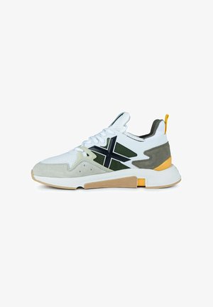 Zapatilla deportiva blanca con detalles en gris y oliva, que presenta una parte superior de malla, elementos de ante texturizado y una suela de goma con un patrón en forma de panal.