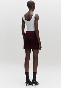 Aansluitend wit tanktop en een geruite minirok in tinten van bordeaux en zwart. De rok heeft een gestructureerd patroon en een hoge tailleband.