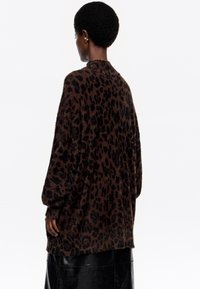 Cárdigan marrón con estampado de leopardo, fabricado con un tejido suave y texturizado, de manga larga y corte holgado, que presenta un cuello redondeado y aberturas laterales.
