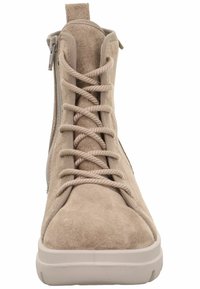 Bota de tobillo de ante beige con suela blanca plana, cordones en la parte delantera y cremallera lateral para un fácil acceso. Presenta una textura suave y una punta redondeada.