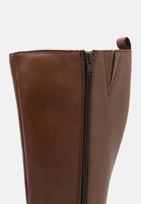 Bottine en cuir marron avec fermeture éclair sur le côté, texture lisse, bout arrondi et accents cousus au bord supérieur.