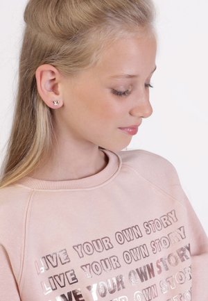 Blush rozen sweatshirt met metallic tekst "LEEF JE EIGEN VERHAAL", ronde halslijn, raglanmouwen, zachte textuur. Kleine vlinderoorbellen.