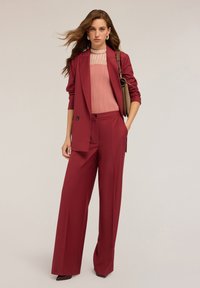 Bordeaux-coloured blazer en wijde broek van soepel materiaal, gecombineerd met een lichtroze geribbelde top en een bruine handtas.