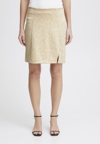 Mini jupe beige avec un motif animal discret, dotée d'une fente sur le côté et d'une texture lisse. Association avec des sandales noires à lanières.