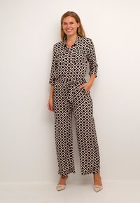 Jumpsuit a fantasia nero e beige con forme a diamante, maniche lunghe, vita elastica, tasche frontali e design a gamba larga.