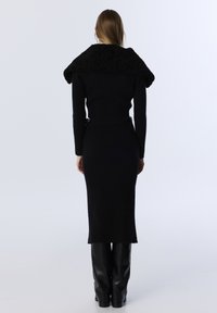 Zwarte geribde gebreide jurk met een oversized textuur kraag, aansluitende silhouet en lange mouwen, gecombineerd met hoogglanzende zwarte laarzen.