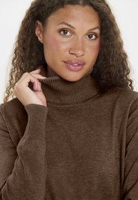 Barna garbónyakú pulóver puha anyagból, bordázott nyakkal és mandzsettával, sima textúrával és testhezálló szabással.