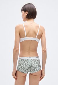 Balta reguliuojama liemenėlė su paprastu dizainu, derinama su žaliais gėlių raštu paltinančiais šortukais, kurių juosmuo baltas su užrašu „PIECES“.