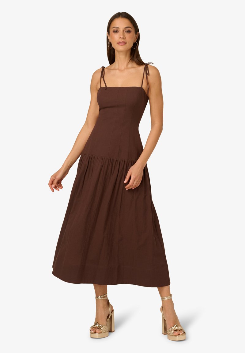 Hnědé, bezramínkové midi šaty s přiléhavým korzetem, rozšířenou sukní a šňůrkovými ramínky; doplněné zlatými sandály na blokovém podpatku.