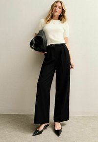 Zwarte wijde broek, zacht wit donzig truitje, zwarte puntige platte schoenen en een grote zwarte handtas. Minimalistische stijl met strakke lijnen.