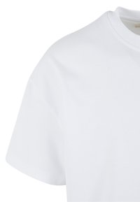 Nahaufnahme eines schlichten weißen Kurzarm-T-Shirts, das die Schulter-, Ärmel- und Kragenpartie vor weißem Hintergrund zeigt.
