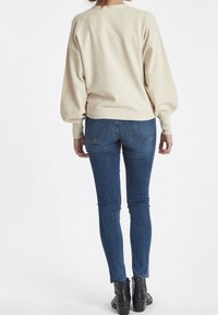 Kermanvärinen, löysiä malli villapaita, jossa on pallo-olkaimet ja ribbireunus, yhdistettynä tummansinisiin tiukkoihin farkkuihin ja mustiin nilkkabootiihin.