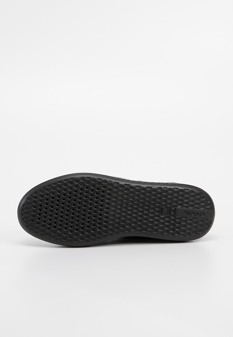 Semelle de chaussure noire avec un motif texturé en forme de nid d'abeille. Présente un logo imprimé et un bord extérieur lisse. Conçue pour l'adhérence et la durabilité.