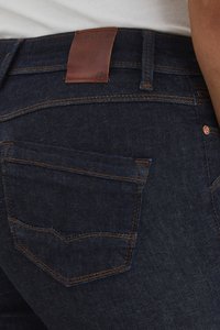 Vaqueros de mezclilla azul oscuro con una etiqueta de cuero en la cintura, detalles de costura prominentes y un bolsillo trasero con un contorno definido.