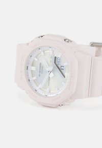 Montre G-Shock avec un boîtier et un bracelet en résine rose. Elle est dotée d'un cadran rond, d'accents blancs et argentés, d'un affichage analogique et numérique, et est résistante à l'eau.