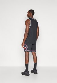 Juoda sportinė raištelė su baltais apdailos elementais, derinama su juodomis kelnių šortais, turinčiais raudoną ir mėlyną logotipą bei geometrinį raštą. Papuošta juodomis kojinėmis ir batais.