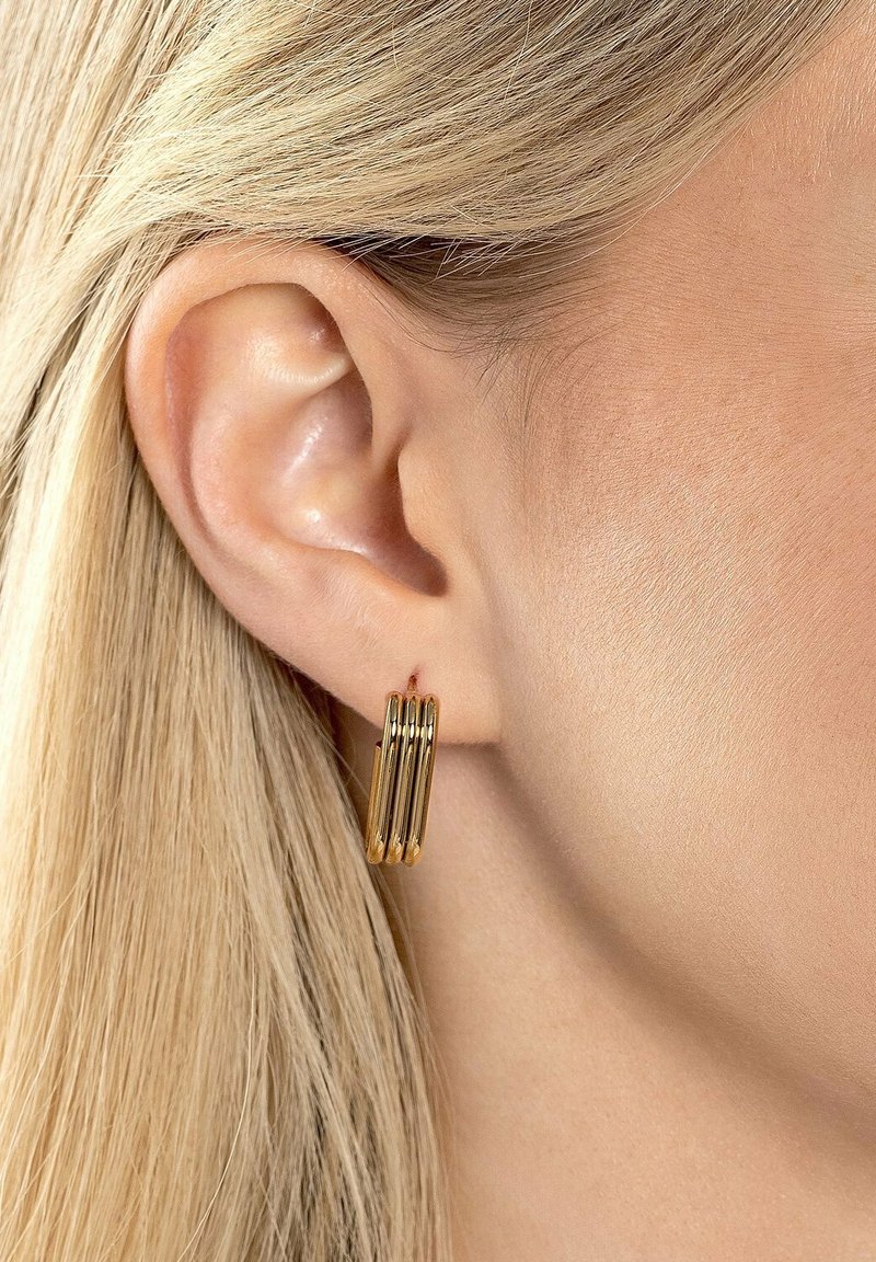 Orecchini a cerchio in oro con un design cilindrico stratificato, appesi all'orecchio, che mostrano una superficie lucida e una texture uniforme.