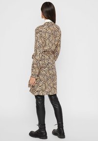 Abito floreale con maniche lunghe, sfondo nero, motivo multicolore, vita con cintura, abbinato a pantaloni in pelle nera e stivali.