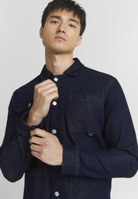 Dark blue denim jacket featuring a collared neckline, snap-button closure, two front pockets, and durable fabric texture.