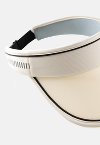 Daszek wykonany z lekkiego, kremowego materiału z elastycznym czarnym wykończeniem, z niebieską regulowaną taśmą i szczelinami wentylacyjnymi po bokach.